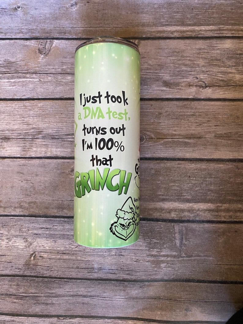 May include: A stainless steel tumbler with a green and white design. The tumbler features the text "I just took a DNA test, turns out I'm 100% that GRINCH" along with a cartoon image of the Grinch.