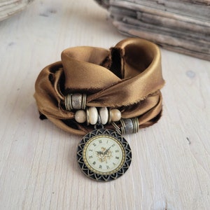 May include: A brown silk scarf with a clock charm and wooden beads. The clock face has Roman numerals and a floral design.