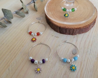May include: Four silver wine glass charms with different colored beads and flower charms. The charms are on a wooden surface.