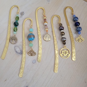 May include: Five gold bookmark pendants with different charms and beads. The charms include a tree, a lotus flower, and a circle with a tree inside. The beads are various colors, including green, blue, brown, and white.