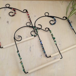 May include: Three black metal bird perches with wooden dowels. Each perch is decorated with colourful beads in shades of red, green, and blue.