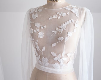 May include: A white sheer top with long sleeves and floral embroidery. The top is made of a lightweight fabric and has a relaxed fit.