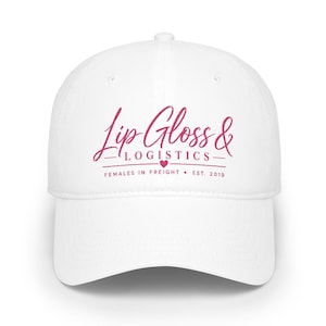 May include: A white baseball cap featuring the dark pink embroidered text Lip Gloss & LOGISTICS with a small heart icon, followed by the text FEMALES IN FREIGHT • EST. 2019 centred on the front panel of the hat.