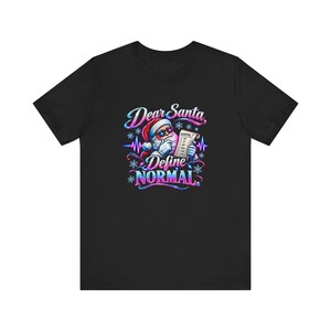 May include: A black short-sleeve t-shirt featuring a graphic of Santa Claus wearing star-shaped sunglasses and holding a checklist. The text reads Dear Santa, Define NORMAL, with a heartbeat line and snowflake accents in blue and pink.