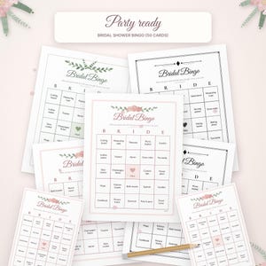 May include: A collection of Bridal Shower Bingo game cards featuring a grid with the letters B-R-I-D-E at the top. The cards include floral accents, a central free space, and various household item text. A wooden pencil lies across the cards.