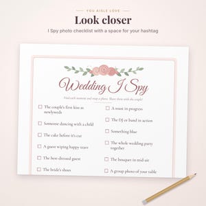 May include: A white Wedding I Spy game card featuring a floral illustration of pink roses and green leaves at the top. The text includes a checklist of photo prompts for guests, such as the couple's first kiss and a toast in progress, with checkboxes next to each item.
