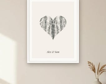 May include: A framed wall art print featuring a black fingerprint heart graphic centred on a cream background. Below the heart, the text Alex & Sam is printed in a black serif font. The artwork is enclosed in a simple white frame.