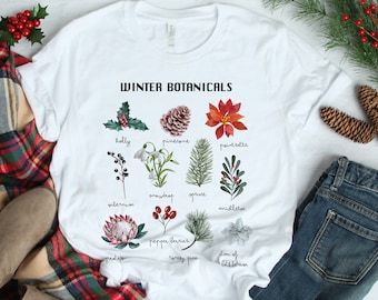 May include: White t-shirt with a graphic of winter botanicals, including holly, poinsettia, snowdrop, and spruce. The text "WINTER BOTANICALS" is printed at the top of the graphic.