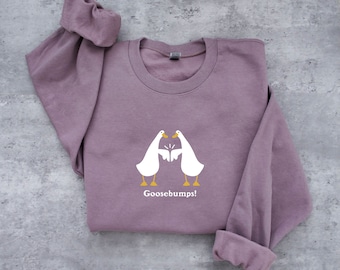 May include: A mauve sweatshirt with a white graphic of two geese facing each other with the text "Goosebumps!" printed below.