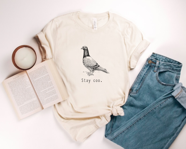 以下が含まれることがあります： クリーム色のTシャツに、白黒の鳩のイラストと「Stay coo.」の文字がプリントされています