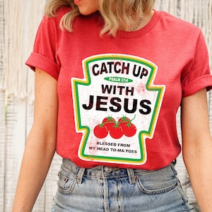 May include: Red t-shirt with a ketchup bottle graphic that says "Catch Up With Jesus" and "Blessed From My Head To-Ma-Toes".