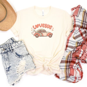 May include: A beige t-shirt with a graphic of a red, orange, and blue vintage car with the text "LOVEBUG" above it. The car has pink hearts around it.