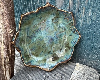 May include: A teal green ceramic dish with a scalloped edge and a decorative design. The dish has a rustic, handmade look.