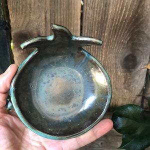 Peut inclure: Un plat en céramique bleu-vert et brun en forme de grenade. Le plat a une finition brillante et un bord légèrement surélevé.