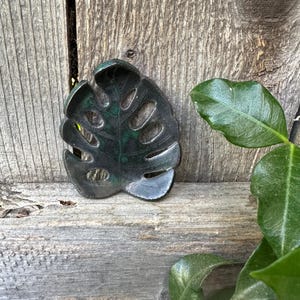 Może przedstawiać: Czarna i zielona ceramiczna miseczka w kształcie liścia z wyciętym wzorem. Miseczka leży na drewnianej powierzchni.