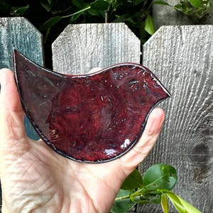 Puede incluir: Un plato de cerámica rojo oscuro en forma de pájaro con un acabado brillante. El plato tiene forma de pájaro con un cuerpo redondeado y un pico puntiagudo.
