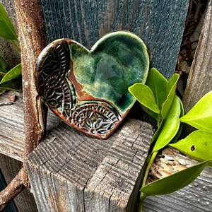 Puede incluir: Un plato de cerámica en forma de corazón con un esmalte verde y detalles marrones. El plato tiene un diseño decorativo en el lateral.