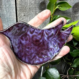 Puede incluir: Un plato de cerámica de color púrpura en forma de pájaro con un esmalte marmoleado y en espiral. El plato tiene forma de pájaro con un cuerpo redondeado y un pico largo y puntiagudo.