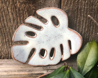 May include: White ceramic monstera leaf dish with brown edges. The dish has a textured surface and is perfect for holding jewelry or other small items.