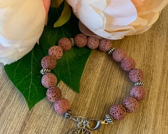May include: A pink lava rock bracelet with a silver tree of life charm. The bracelet is made of small, round beads and has a silver clasp.