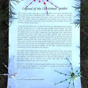 May include: A white card with blue text explaining the legend of the Christmas spider. The text describes how spiders were banished from a house being cleaned for Christmas Eve, but then crept back to see the decorated tree. The text says that the Christ child touched the spider webs, turning them to sparkling silver and gold. The card also shows a red and white beaded spider ornament and a green beaded spider ornament.