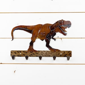 May include: A metal dinosaur key holder with a brown and black finish. The dinosaur is standing on a metal base with five hooks.