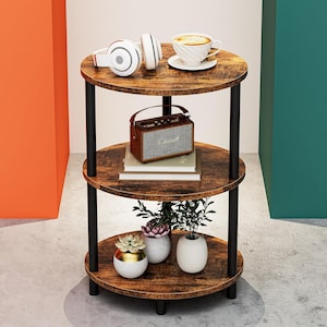 May include: A three-tier round side table with a dark wood grain finish and black metal supports. The top shelf holds white headphones and a white coffee cup. The middle shelf features a brown Marshall speaker on books. The bottom shelf holds three small potted plants.