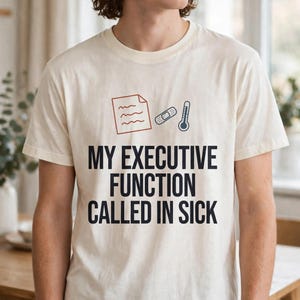 May include: An off-white t-shirt featuring a graphic of a document, a bandage, and a thermometer above the black text that reads: MY EXECUTIVE FUNCTION CALLED IN SICK. The shirt has a crew neckline and short sleeves.