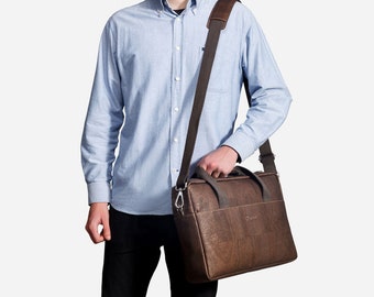 May include: A brown leather briefcase with a shoulder strap. The briefcase has a zipper closure and a small pocket on the front.