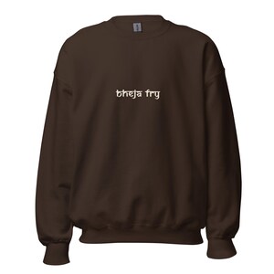 Op de afbeelding: Een donkerbruin sweatshirt met ronde hals en de tekst "bheja fry" in een lichte crèmekleur gedrukt in het midden van de borst. Het kledingstuk heeft lange mouwen met geribbelde boorden en een geribbelde zoom in een eenvoudig ontwerp.