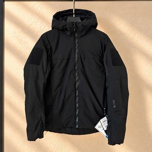 May include: A black hooded jacket featuring a full-length front zipper, long sleeves with rectangular hook-and-loop patches on the shoulders, and a small logo on the left sleeve cuff. A white product tag with the text GO is attached.
