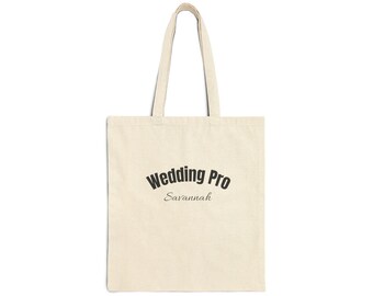 May include: A beige canvas tote bag with two shoulder straps. The front features the black text Wedding Pro in a bold, arched font, with the word Savannah printed underneath in a smaller, elegant, cursive-style script font.