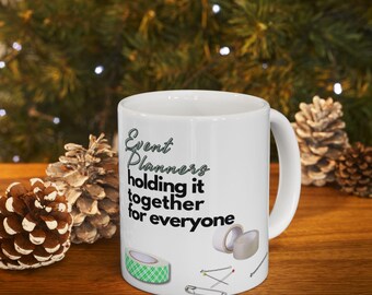 May include: A white ceramic mug featuring the black text Event Planners holding it together for everyone. The design includes illustrations of a green patterned adhesive tape roll, a white tape roll, sewing pins, and a silver paperclip.