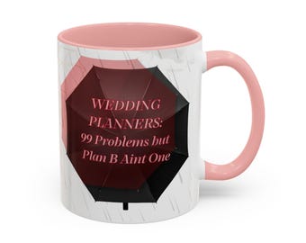 May include: A white ceramic mug with a soft pink interior and handle. The exterior features a graphic of a dark red and black umbrella against a light gray background with rain streaks. The text reads: WEDDING PLANNERS: 99 Problems but Plan B Aint One.