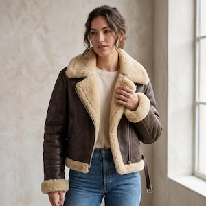 Peut inclure: Une veste en cuir marron foncé dotée d'une épaisse doublure en fausse fourrure crème, d'un large col cranté, de manches longues avec poignets en fourrure, d'une fermeture éclair argentée et d'une sangle à boucle réglable à l'ourlet.