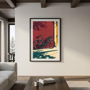 Op de afbeelding: Een ingelijste kunstdruk met een donkere fiets die tegen een felrode muur leunt. De sc&egrave;ne bevat een geel verticaal accent, diepe schaduwen van gebladerte en een lichte ondergrond, alles weergegeven in een grafische illustratiestijl.