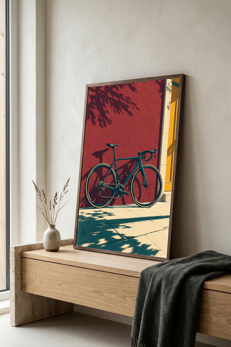 Op de afbeelding: Een ingelijste wandkunstprint met een donkergekleurde racefiets geparkeerd tegen een dieprode muur met een geel deurkozijn. De sc&egrave;ne toont fel zonlicht dat lange, duidelijke schaduwen werpt van de fiets en het nabijgelegen gebladerte.