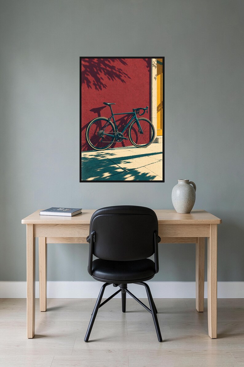 Op de afbeelding: Een ingelijste kunstprint met een donkerblauwe racefiets die tegen een felrode muur leunt. De sc&egrave;ne bevat een geel deurkozijn en duidelijke schaduwen die door de fiets en het gebladerte op de grond en de muur worden geworpen.