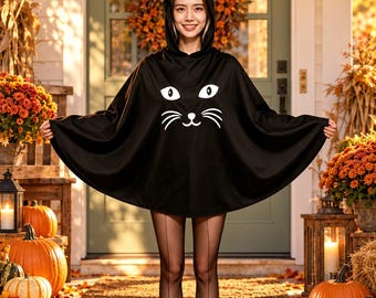 May include: A black hooded cape featuring a white cat face graphic with eyes, whiskers, and a nose on the front, and two small white cat ears attached to the hood. The text PUMPKIN PARTY is printed in orange above the cape.