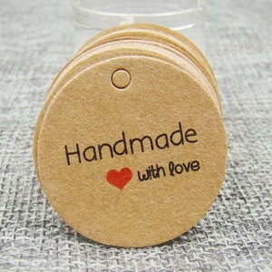 May include: A stack of round, brown kraft paper gift tags with a hole at the top. The tags have the text "Handmade with love" printed in black with a red heart.