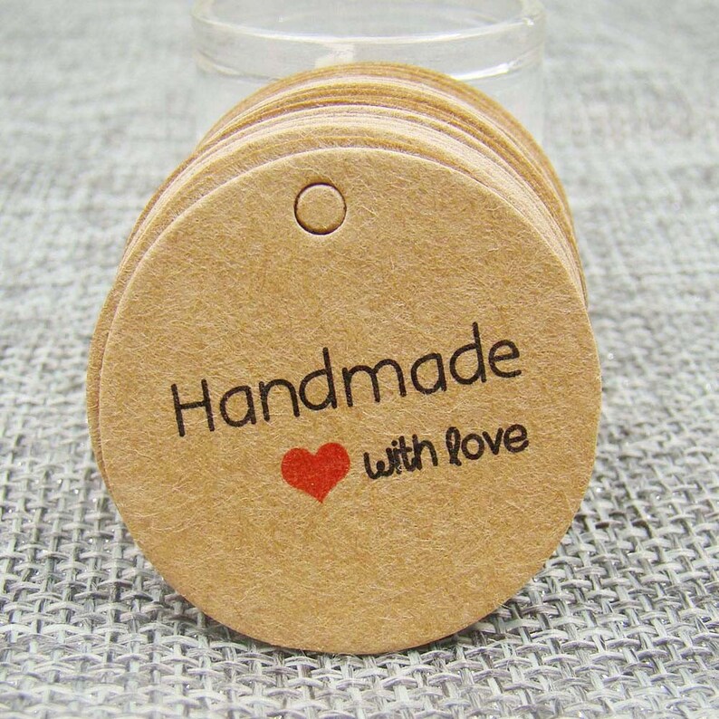 May include: A stack of round, brown kraft paper gift tags with a hole at the top. The tags have the text "Handmade with love" printed in black with a red heart.
