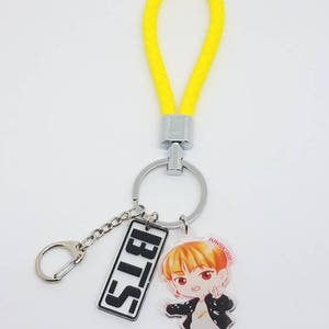May include: A yellow keychain with a silver ring and a black and white rectangular charm with the text "BTS" and a cartoon character charm with the text "JUNGKOOK".