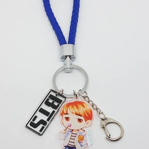 May include: A blue braided keychain with a silver ring and a charm featuring a cartoon character with the word "BTS" on a silver rectangle.
