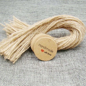 May include: A stack of round, brown kraft paper gift tags with a hole punched at the top. The tags have the text "Handmade with love" printed in black with a small red heart.