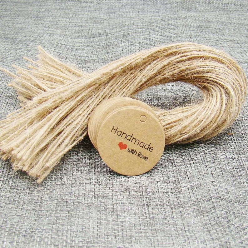 May include: A stack of round, brown kraft paper gift tags with a hole punched at the top. The tags have the text "Handmade with love" printed in black with a small red heart.