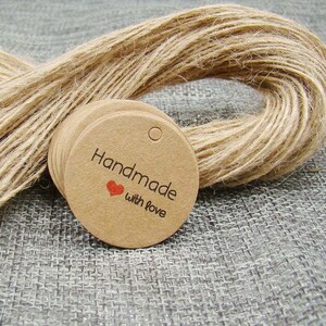 May include: A stack of round, brown kraft paper gift tags with a hole punched at the top. The tags have the text "Handmade with love" printed in black with a small red heart symbol.