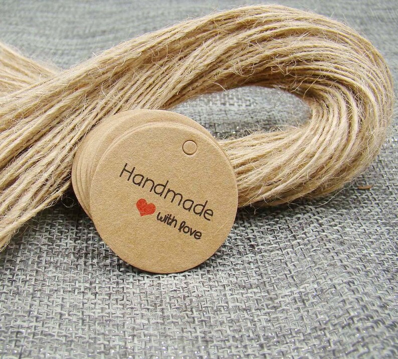 May include: A stack of round, brown kraft paper gift tags with a hole punched at the top. The tags have the text "Handmade with love" printed in black with a small red heart symbol.