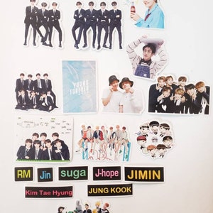 May include: A collection of stickers featuring a K-pop boy band. The stickers are printed on white paper and feature various images of the band members, including individual portraits, group photos, and cartoon illustrations. The stickers also include text such as "Young Forever", "RM", "Jin", "Suga", "J-Hope", "Jimin", "Kim Tae Hyung", and "Jung Kook".