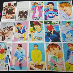 May include: A set of 12 photo cards featuring a K-pop boy band. The cards are printed on white cardstock and feature various images of the band members in different poses and outfits. The cards are all in a similar style, with a white border and a blue background. The band members are wearing colorful clothing and hats, and some are holding props such as watermelons and sunglasses. The cards are perfect for fans of the band or for collectors of K-pop memorabilia.