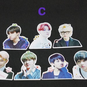 May include: Seven colourful stickers featuring different members of a K-pop band. Each sticker has a white border and features a different member with a unique expression and background. The stickers are printed with the band member's name and a small graphic.
